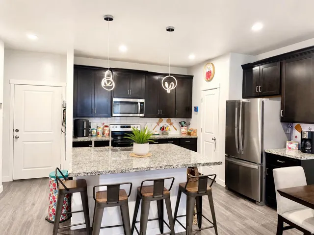 Kitchen featuring wood-finish flooring, dark wood cabinetry, stainless steel appliances, granite countertops, and recessed lighting