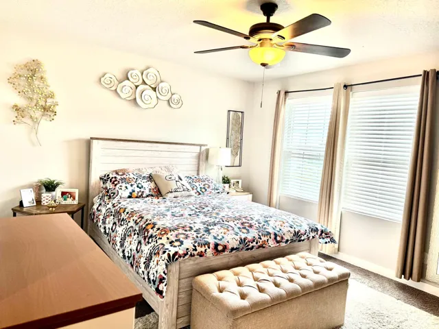 Ceiling fan with integrated lighting, two windows with blinds, and carpeted flooring