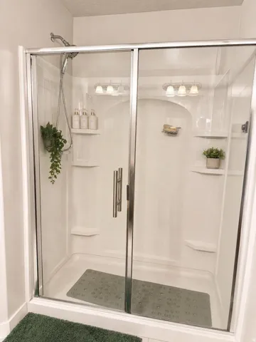 Enclosed shower with a glass door, built-in shelving, and a chrome handheld shower fixture