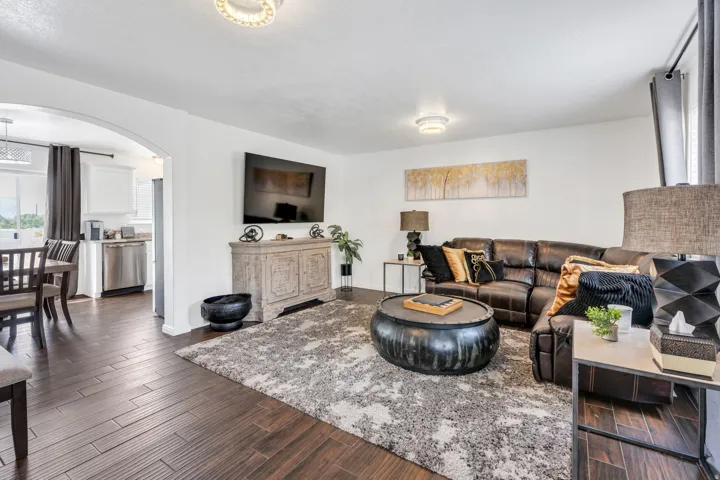 Wood-finish flooring throughout, with an arched entryway leading to the kitchen featuring stainless steel appliances and white cabinetry
