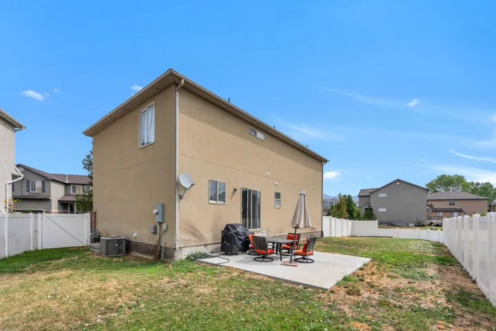 Expansive backyard featuring a concrete patio, white privacy fencing, and a stucco exterior