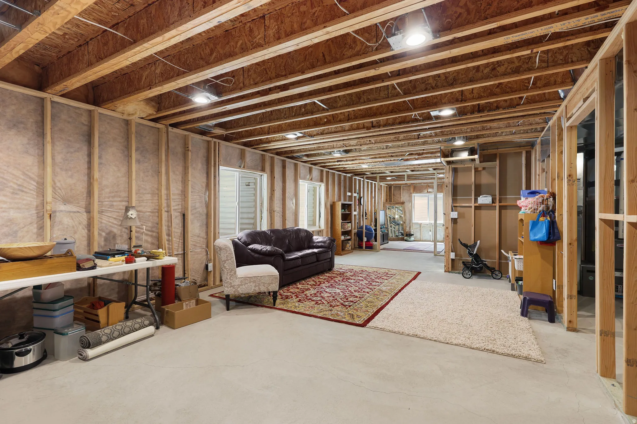 Unfinished basement featuring exposed wood framing, concrete flooring, and multiple window openings