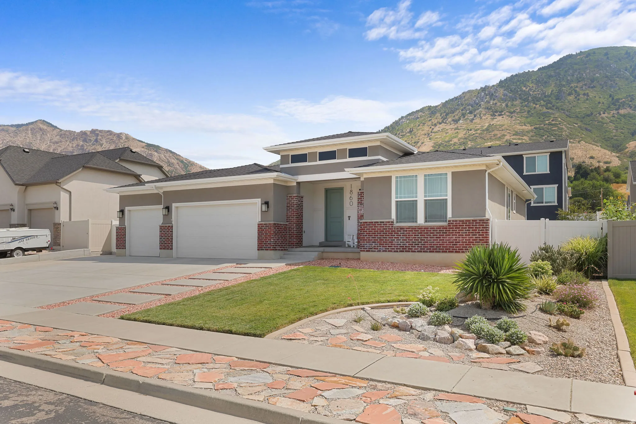 Contemporary stucco and brick exterior with a low-slope roof, dual garage doors, a front lawn, and a xeriscaped garden bed