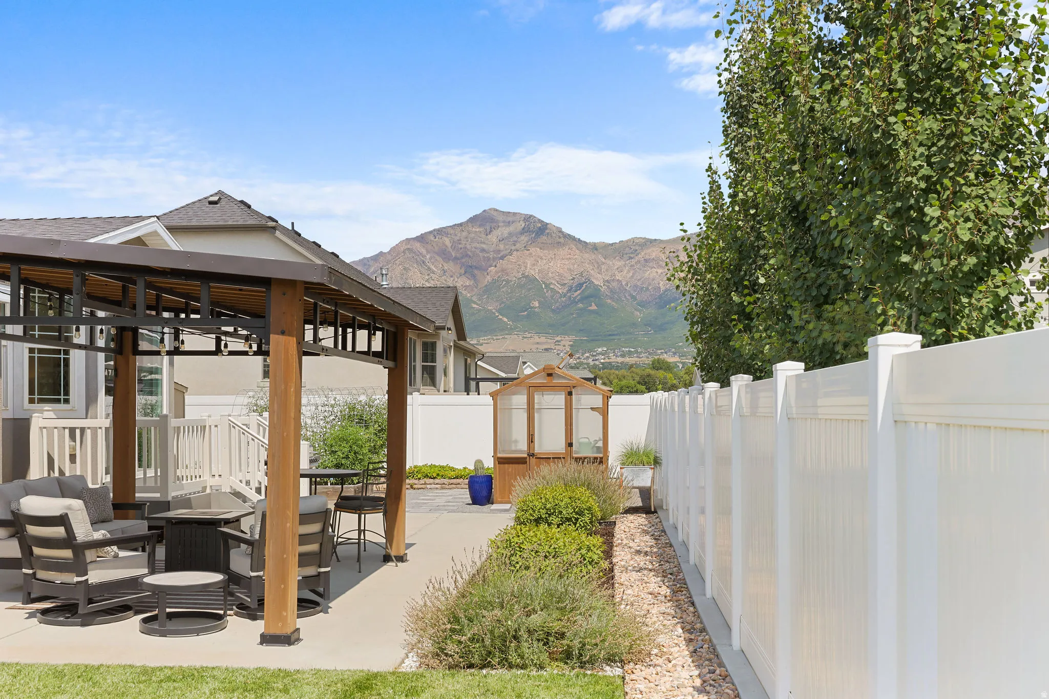 Paved patio with a wood-frame pergola, white privacy fence, and cultivated landscaping