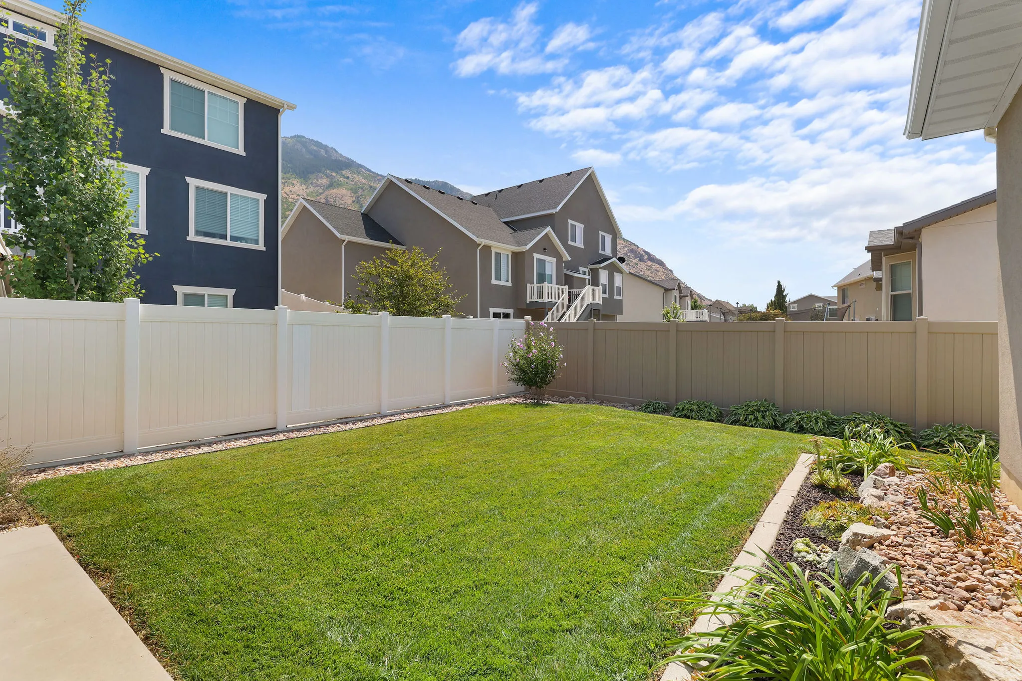 Expansive backyard featuring a manicured lawn, white privacy fencing, and a decorative garden bed with natural rock elements