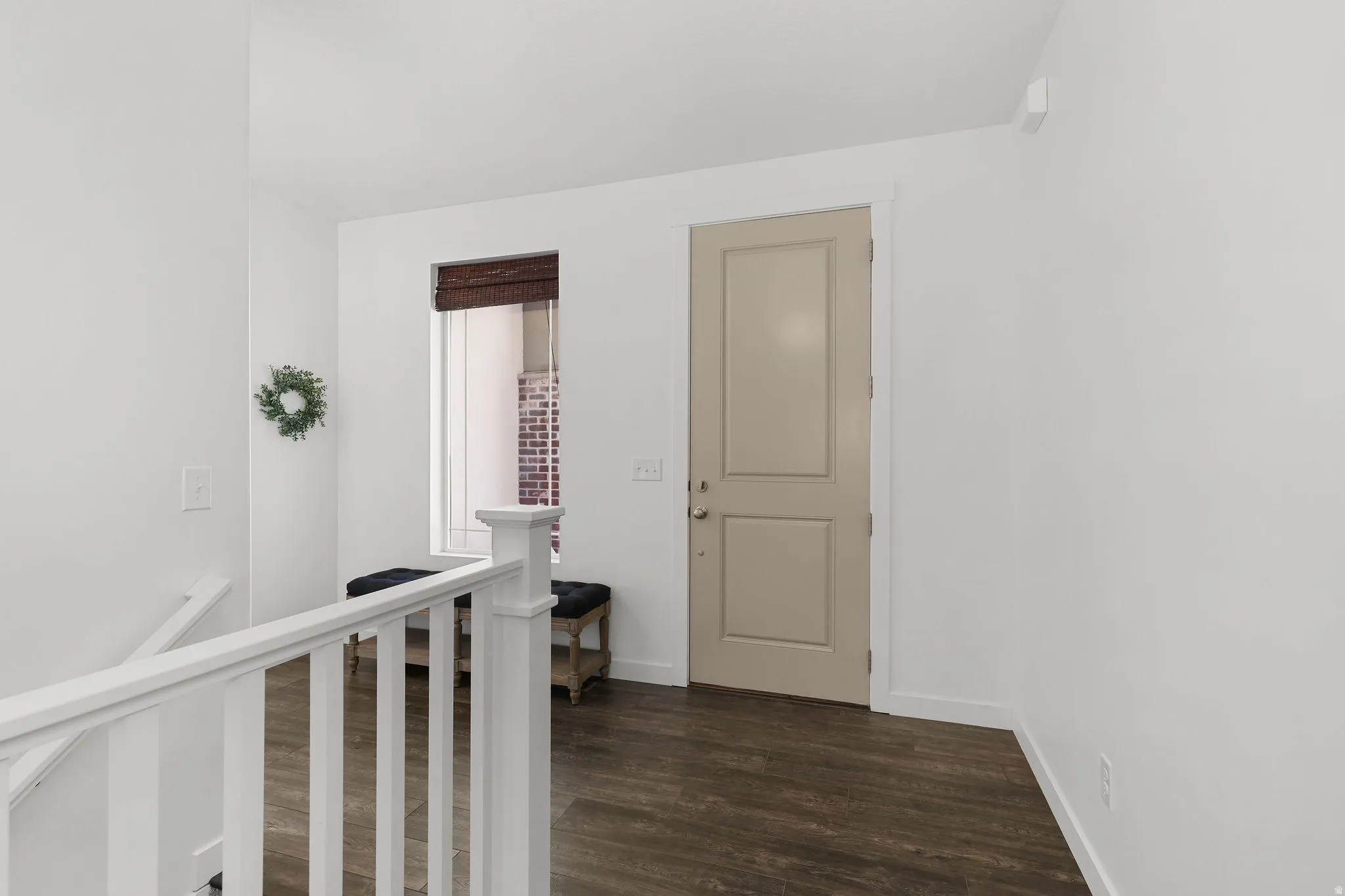 Hardwood-finish flooring, white walls, white railing, natural light from a window, and a paneled entry door