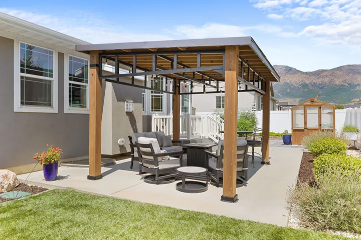 Backyard featuring a covered patio, concrete hardscaping, manicured lawn, and mountain scenery