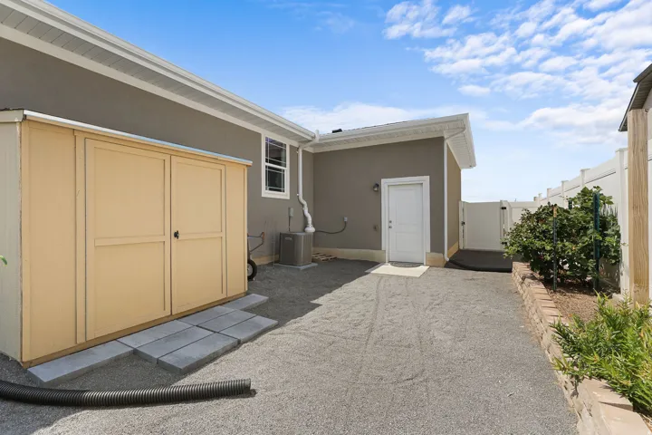 Exterior storage shed with double doors, gravel ground cover, a privacy fence, and an exterior entry door