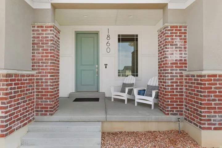 Front entry with a light green door, red brick detailing, concrete porch, and vertical house numbers