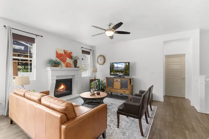 Living area featuring a fireplace with a mantel, multiple windows, a ceiling fan with integrated lighting, and wood-finish flooring