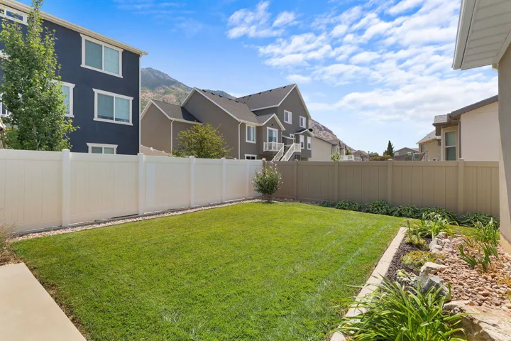 Expansive backyard featuring a manicured lawn, white privacy fencing, and a decorative garden bed with natural rock elements