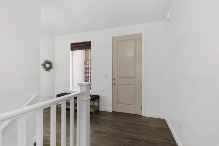 Hardwood-finish flooring, white walls, white railing, natural light from a window, and a paneled entry door