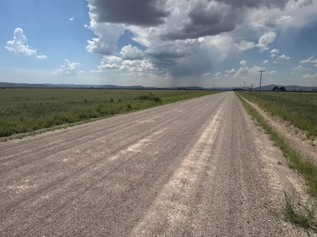 Gravel road with expansive green fields and distant mountains