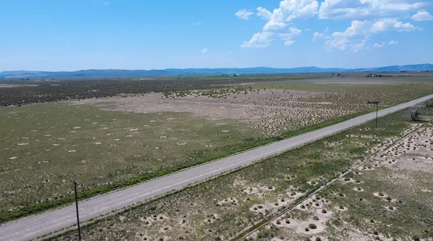 Expansive undeveloped land featuring a clear roadway, natural ground cover, and distant mountainous terrain under a broad sky
