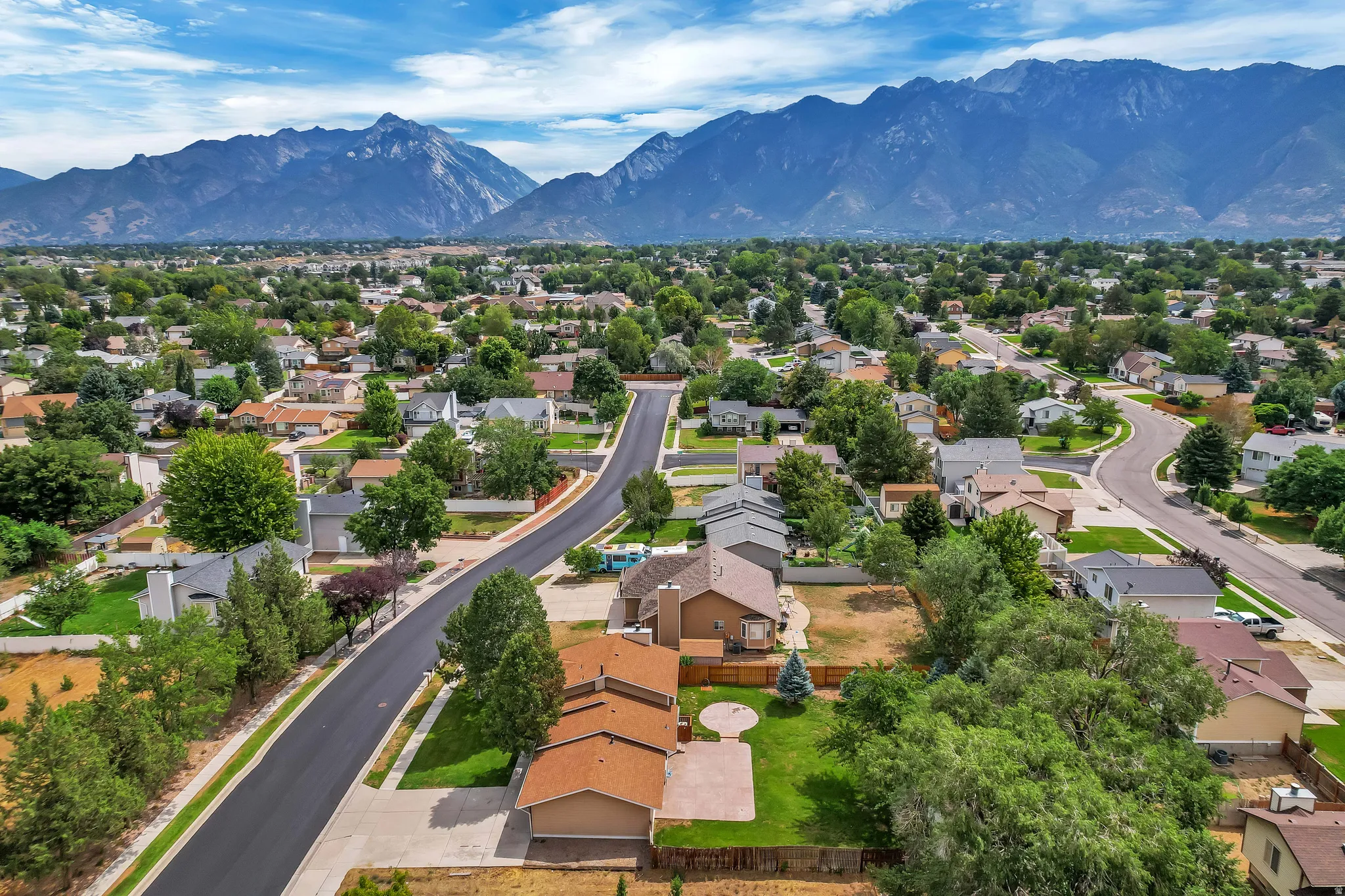 Residential neighborhood featuring mature trees, paved streets, and mountain backdrop