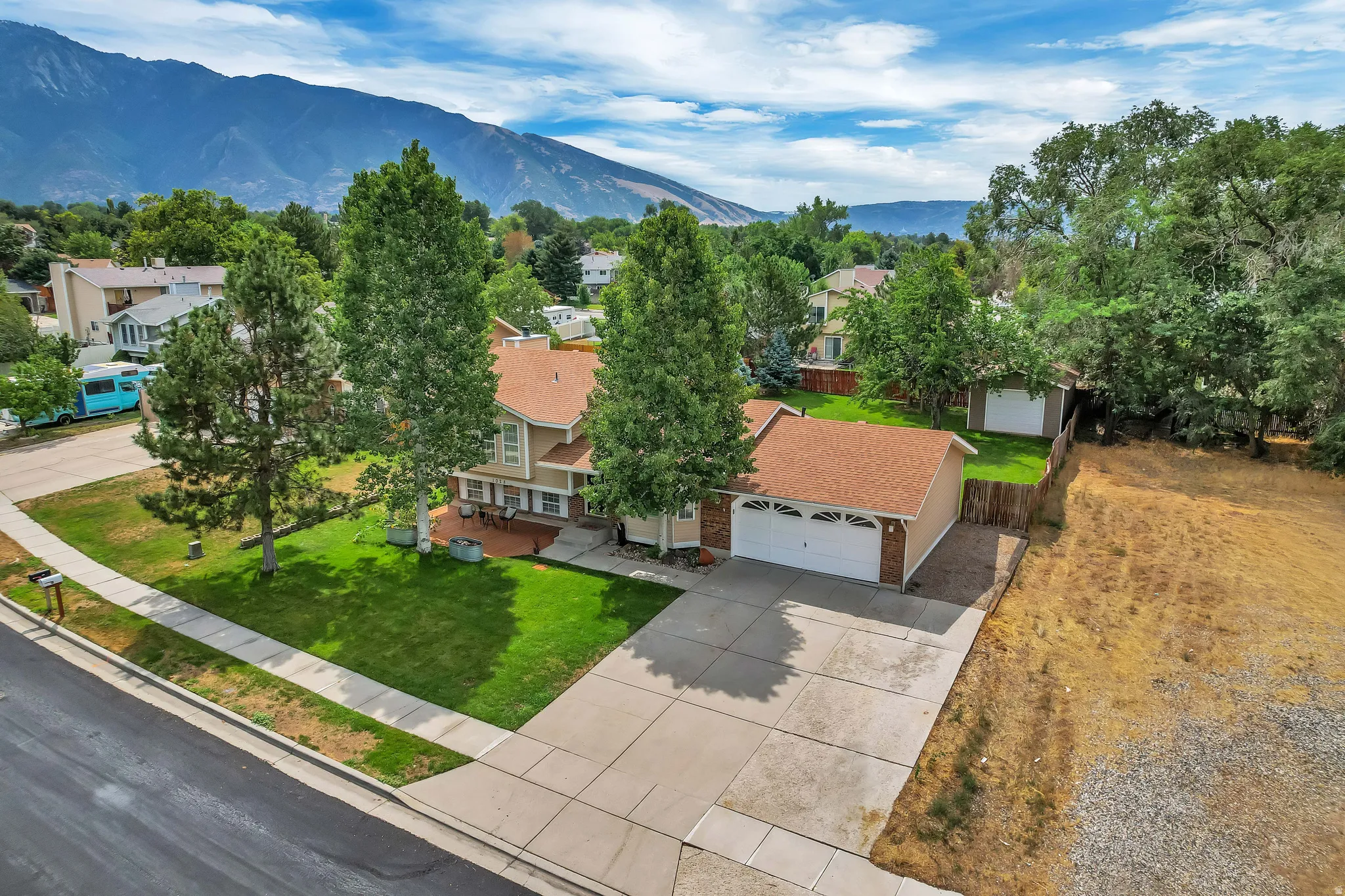 Multi-level residence featuring an attached two-car garage, mature landscaping, and a mountain backdrop