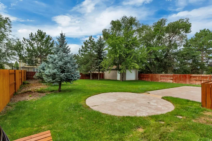 Expansive backyard featuring a manicured lawn, concrete patio, mature trees, and privacy fencing