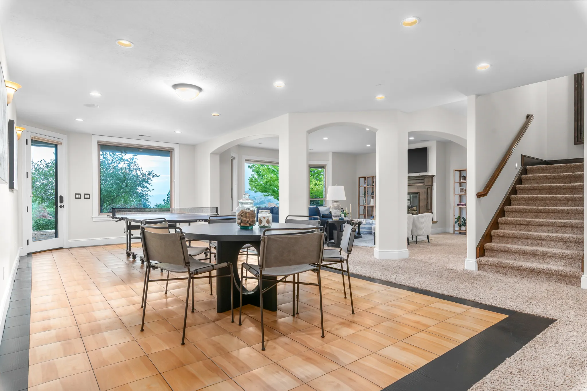 Lower level featuring mixed flooring, arched doorways, multiple recessed lights, a glass-paned exterior door, and a carpeted staircase with wood railing