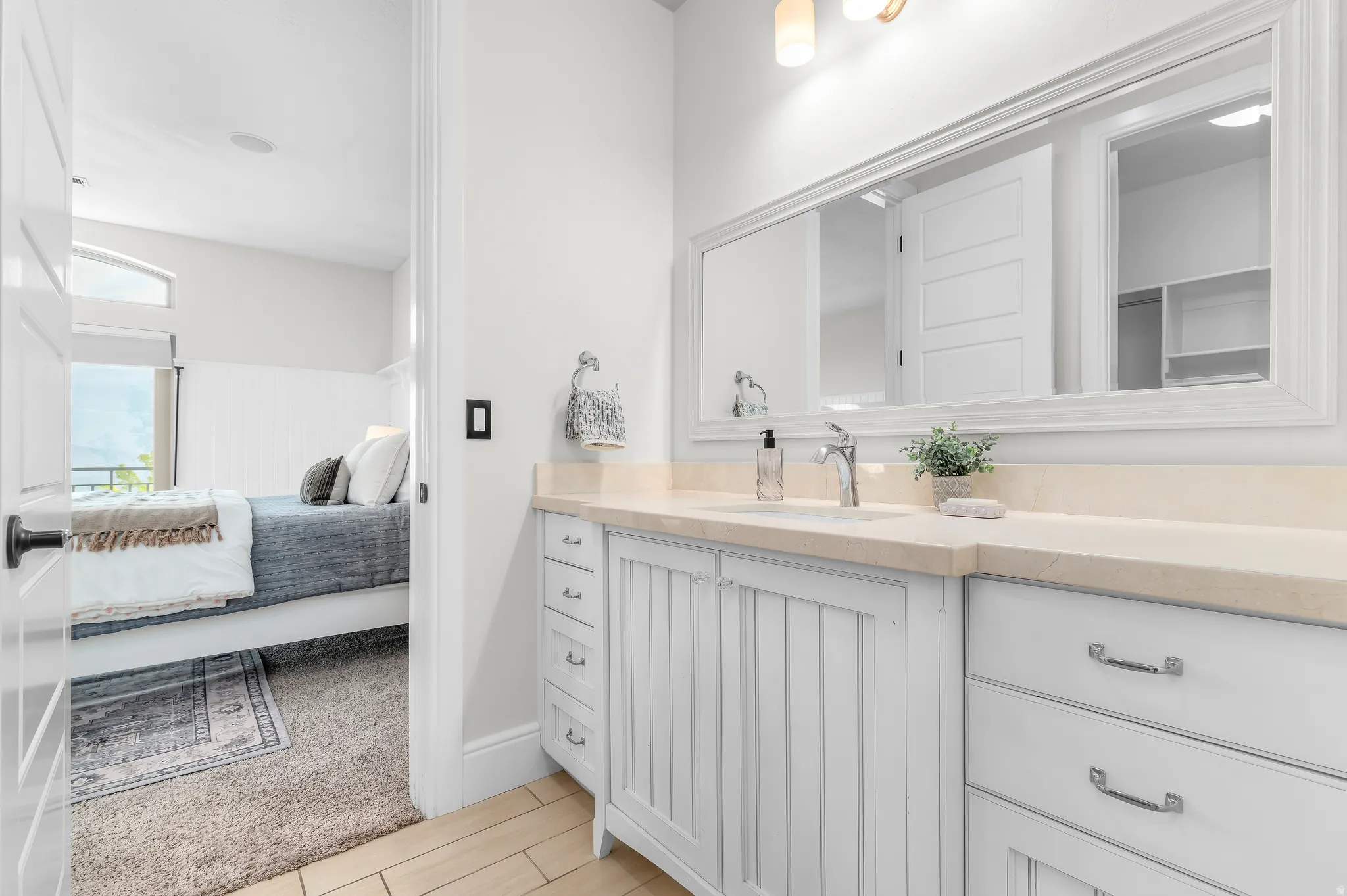 White vanity with beadboard cabinetry, beige countertop, and a large framed mirror