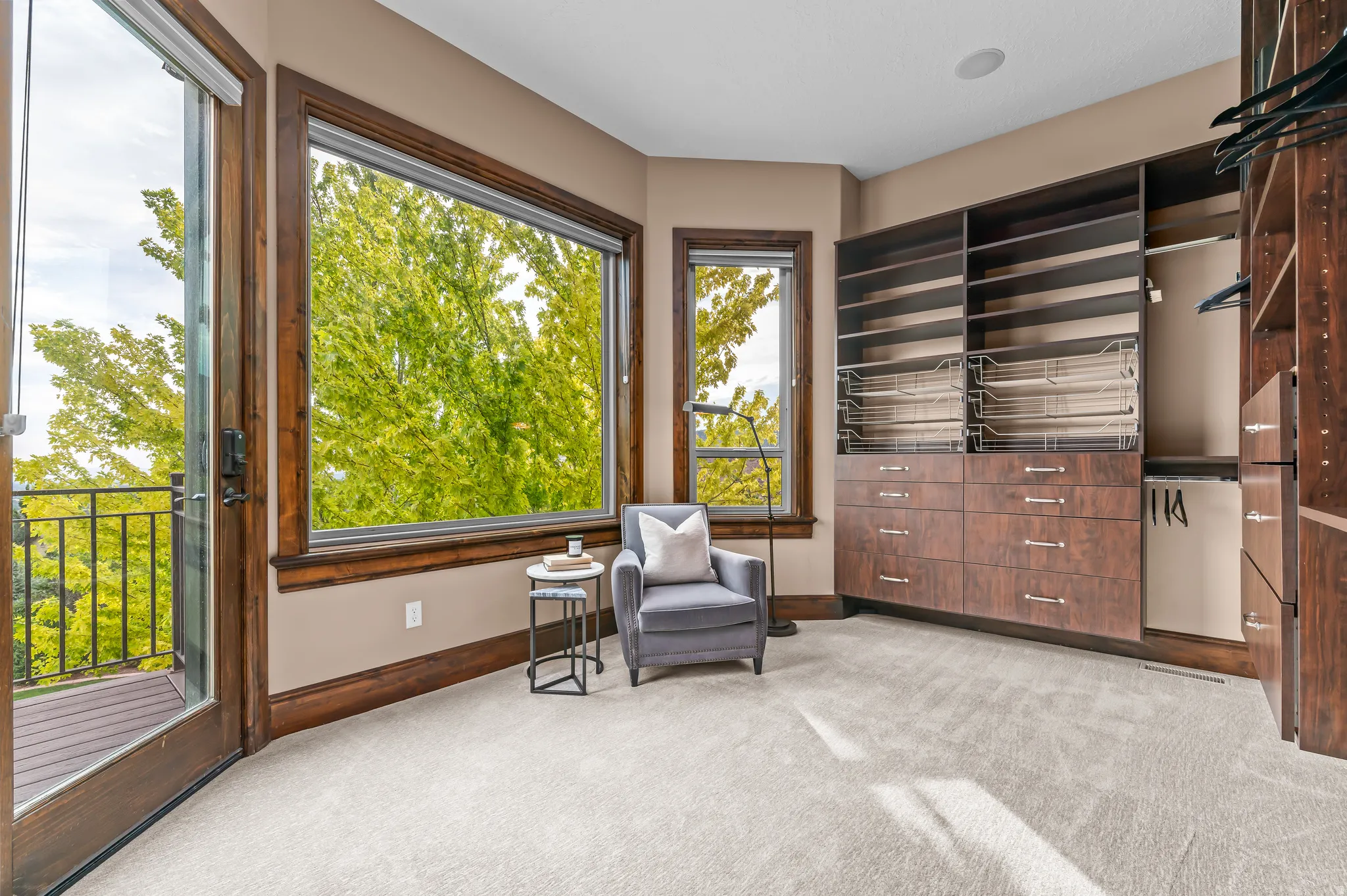 Built-in custom cabinetry with shelving and drawers, large picture window, glass door to a balcony with metal railing, and light-colored carpeting
