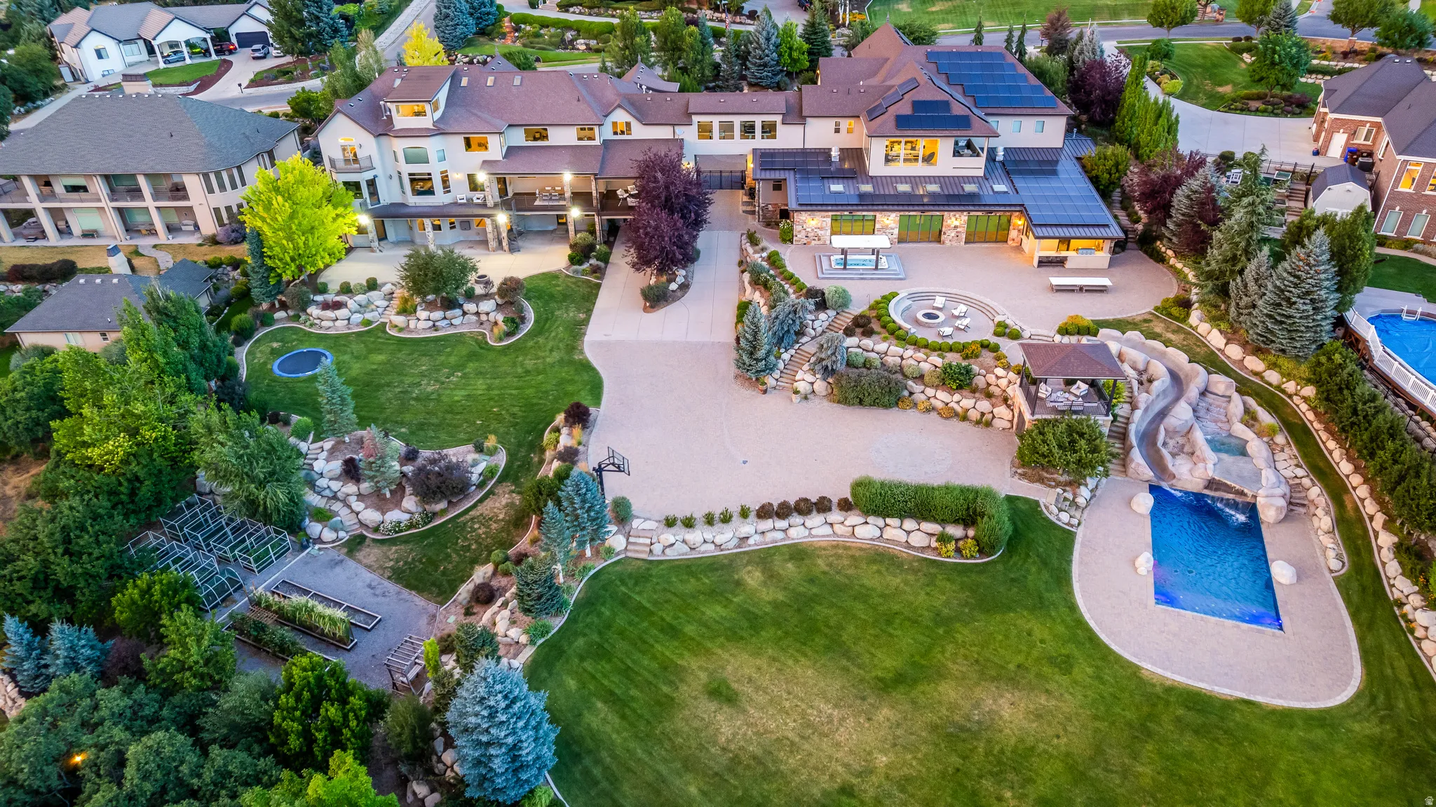 Expansive private grounds featuring a large pool with rock slide, a separate fire pit seating area, multiple manicured lawn areas, established landscaping, and an extended driveway