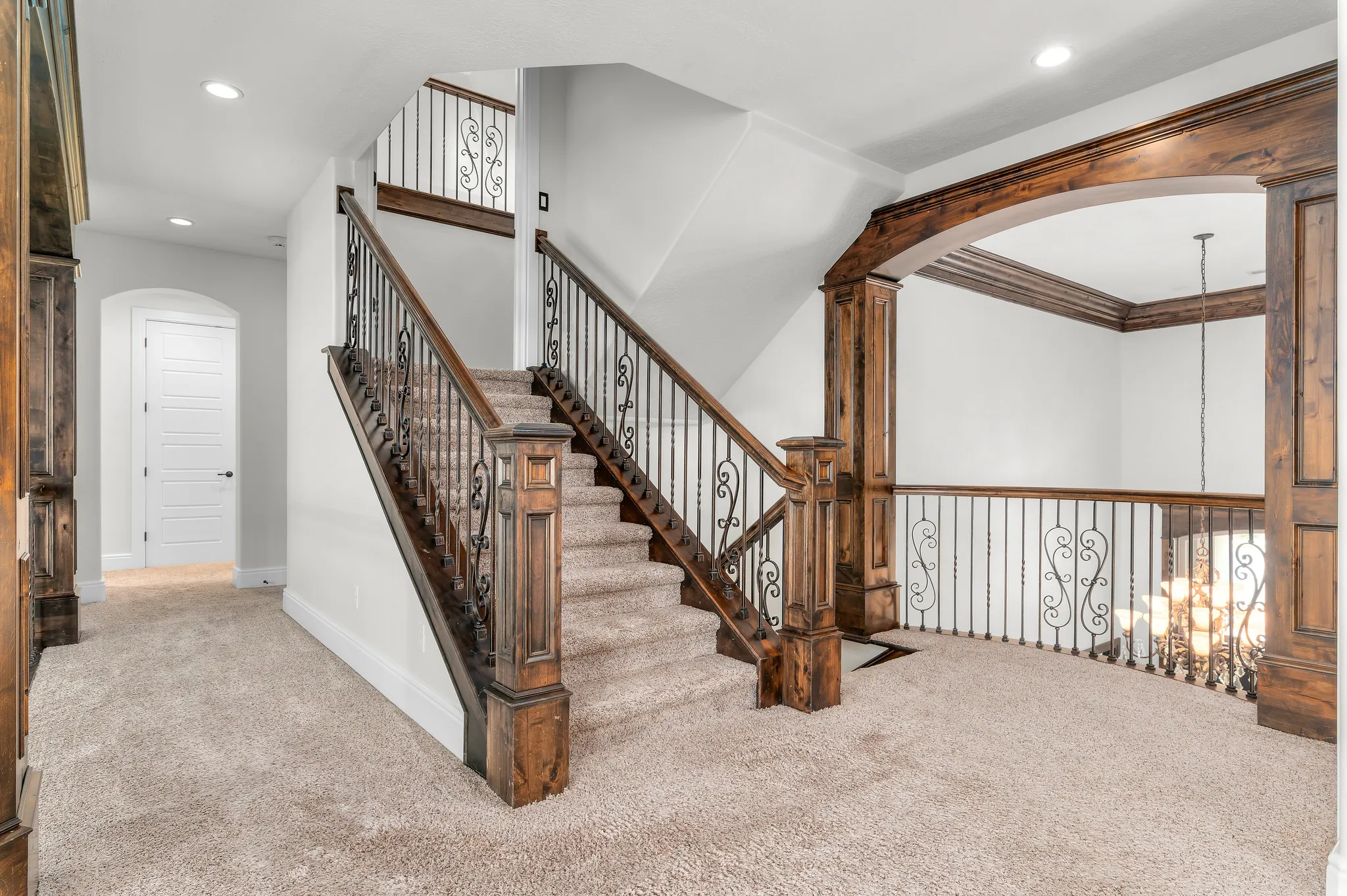 Staircase featuring wood-finish newel posts and railings with wrought iron balusters