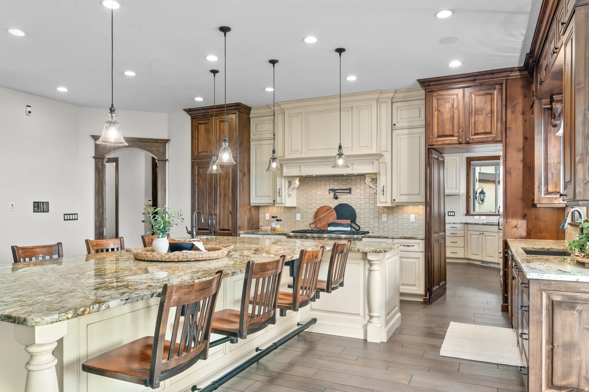 Expansive kitchen island with a stone countertop, recessed lighting, pendant light fixtures, wood-finish flooring, and two-tone cabinetry