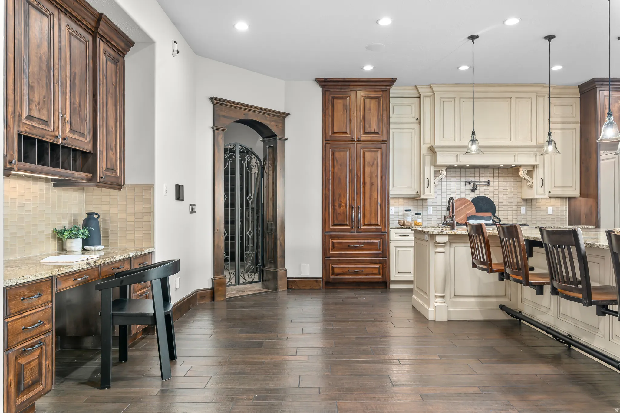 Wood-finish flooring throughout, custom built-in desk area with wood cabinetry, arched entryway with wrought iron gate, built-in pantry storage, and a kitchen island with seating