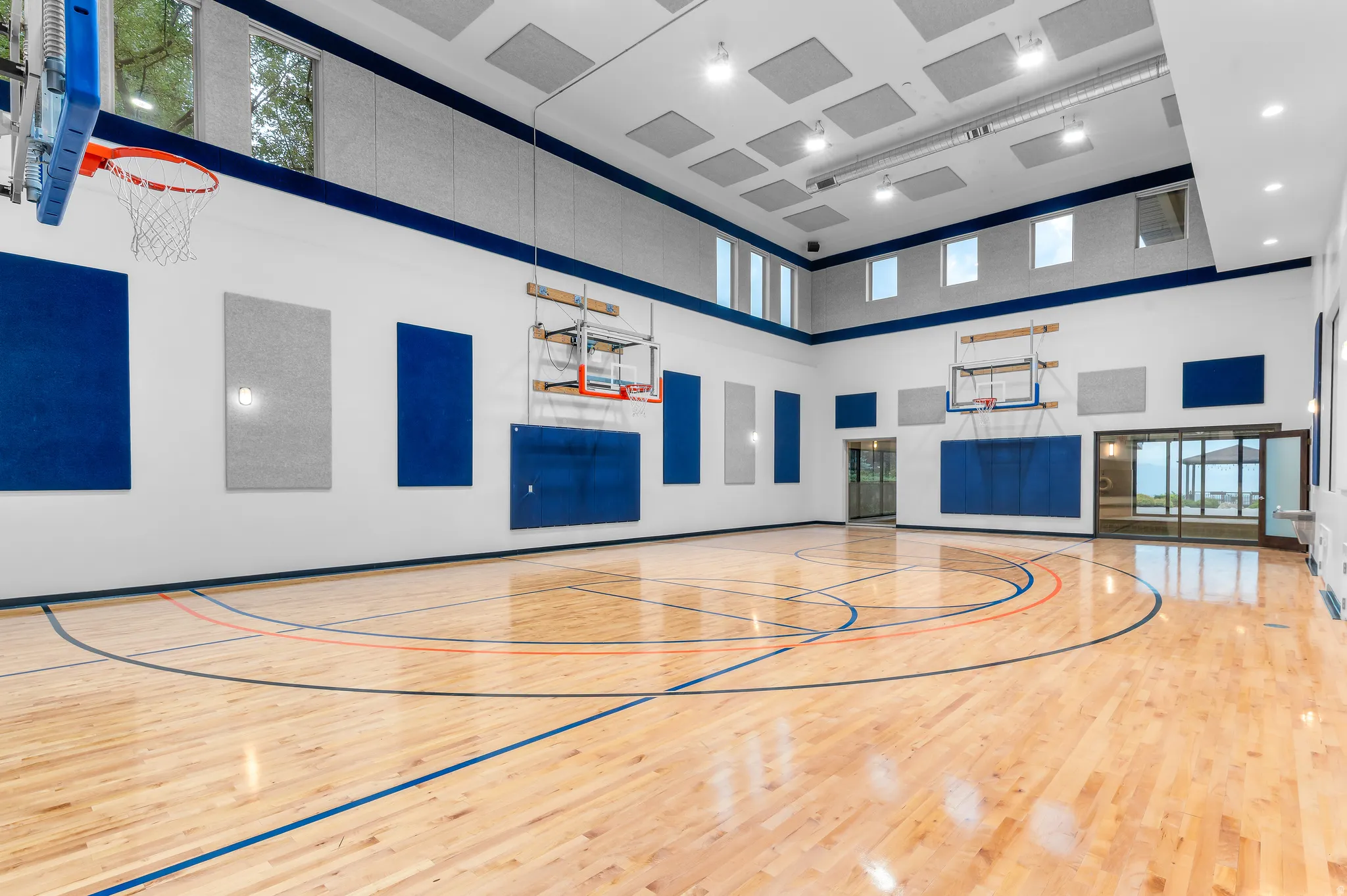 Indoor basketball court with polished hardwood flooring, multiple basketball hoops, high ceilings, acoustic wall panels, and integrated overhead lighting