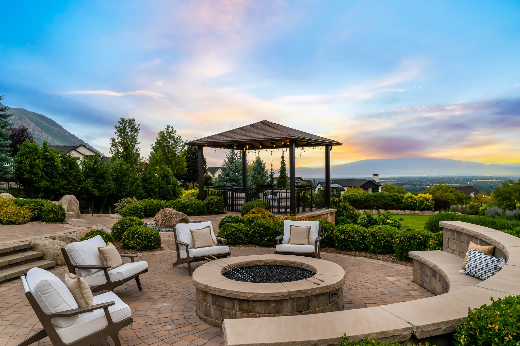 Paver patio featuring a built-in stone fire pit, curved stone bench seating, and a covered gazebo