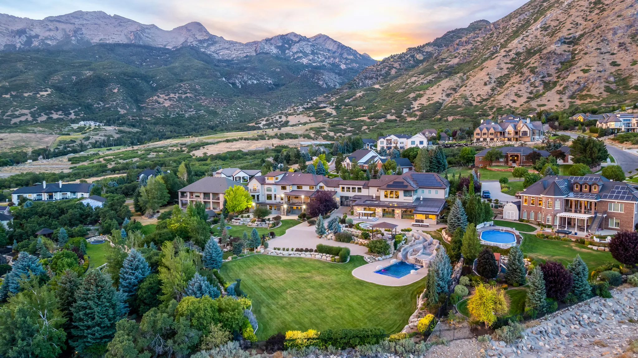 Expansive property with multiple pools, a verdant lawn, mature trees, and a mountain backdrop