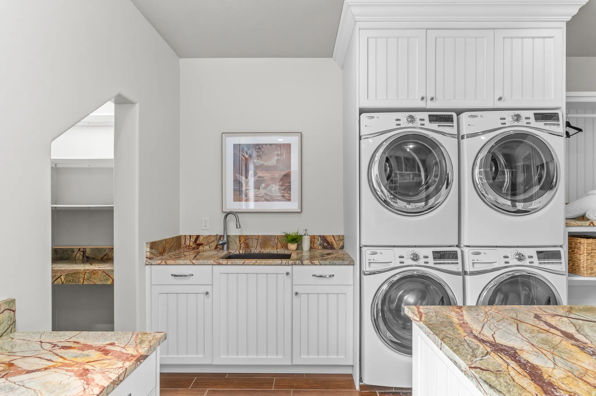 Laundry area featuring white cabinetry, integrated sink, stone countertops, and wood-finish flooring