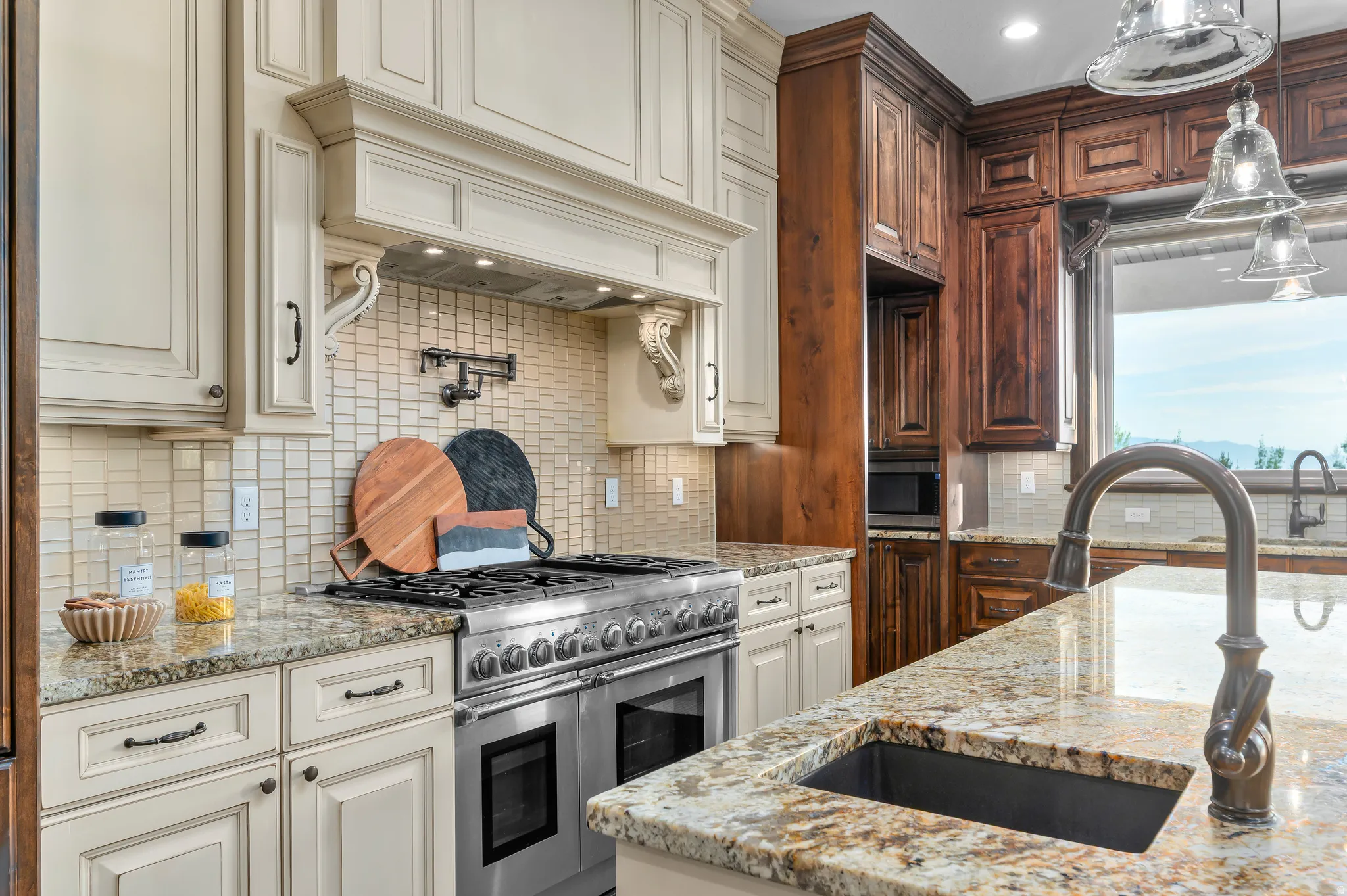 Gourmet kitchen featuring a stainless steel range, light-toned cabinetry, dark wood-finish cabinetry, patterned tile backsplash, and stone countertops