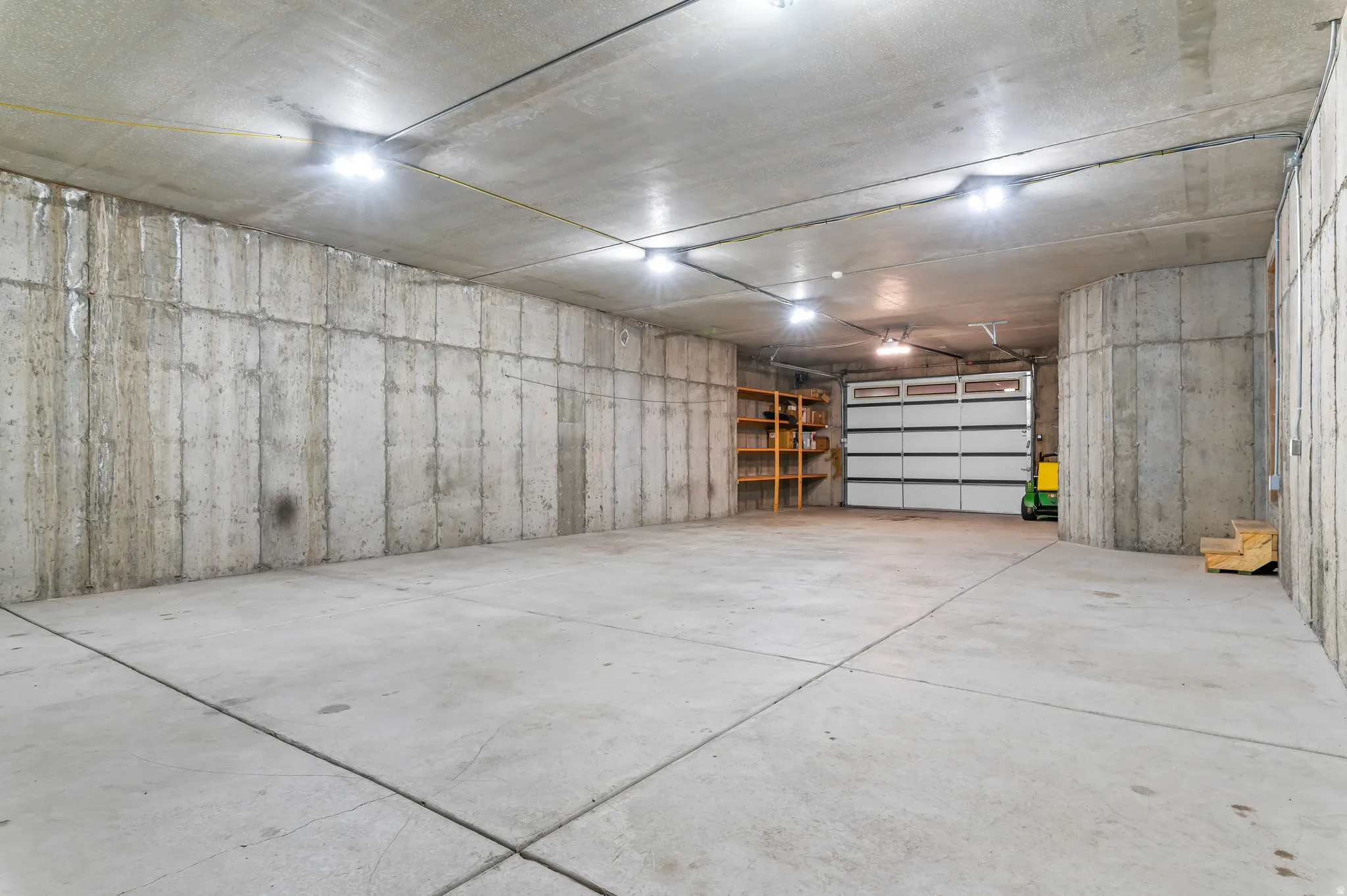 Concrete flooring, concrete walls, overhead lighting, garage door, built-in shelving
