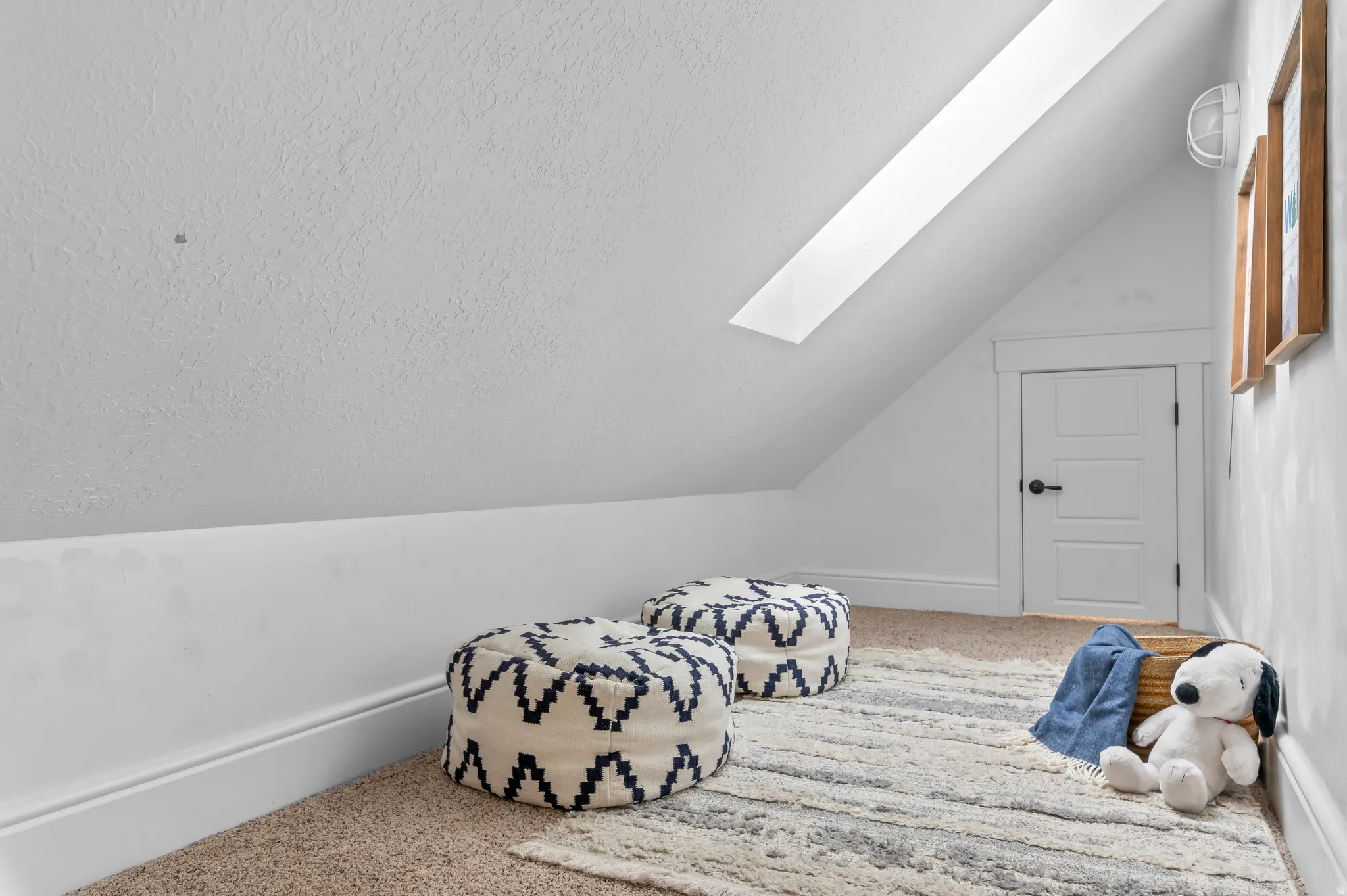 Angled ceiling featuring a skylight, panel door with a matte black handle, and carpet flooring
