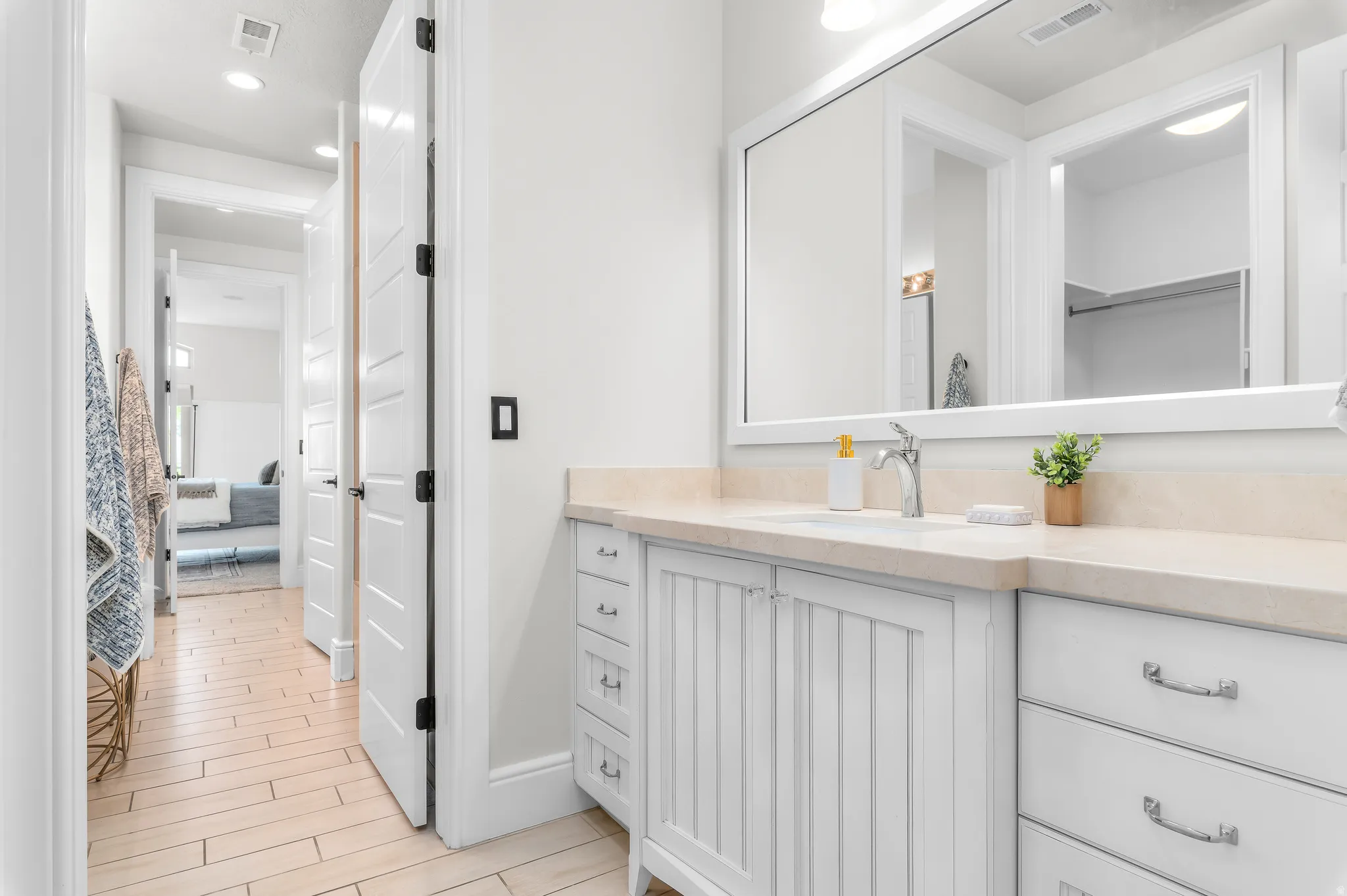 Vanity with a polished chrome faucet, stone countertop, integrated sink, and white cabinetry featuring both drawers and beadboard doors