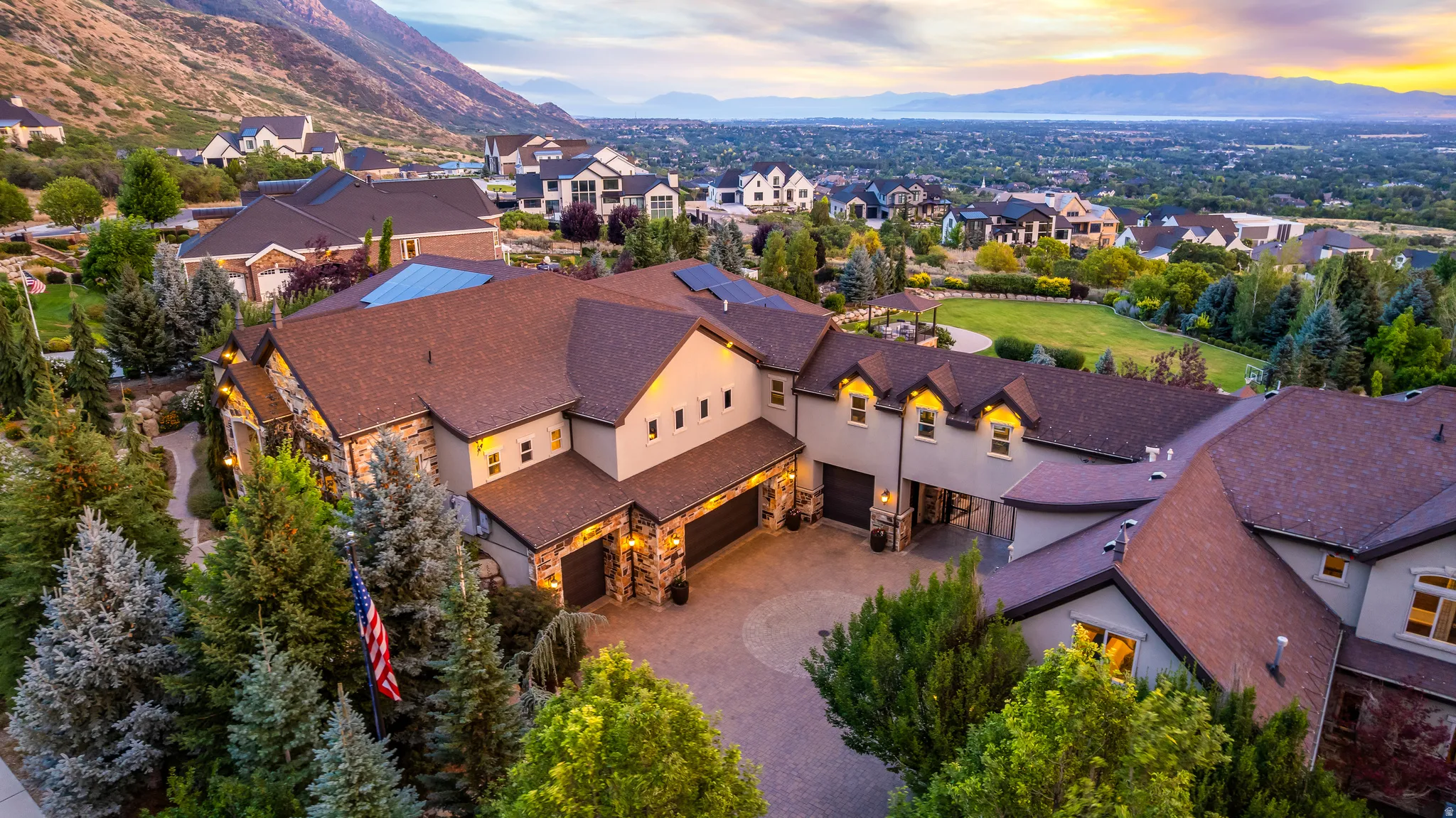 Expansive property featuring a multi-level roofline, stone and stucco exterior, multiple garage bays, a circular driveway, and mature landscaping
