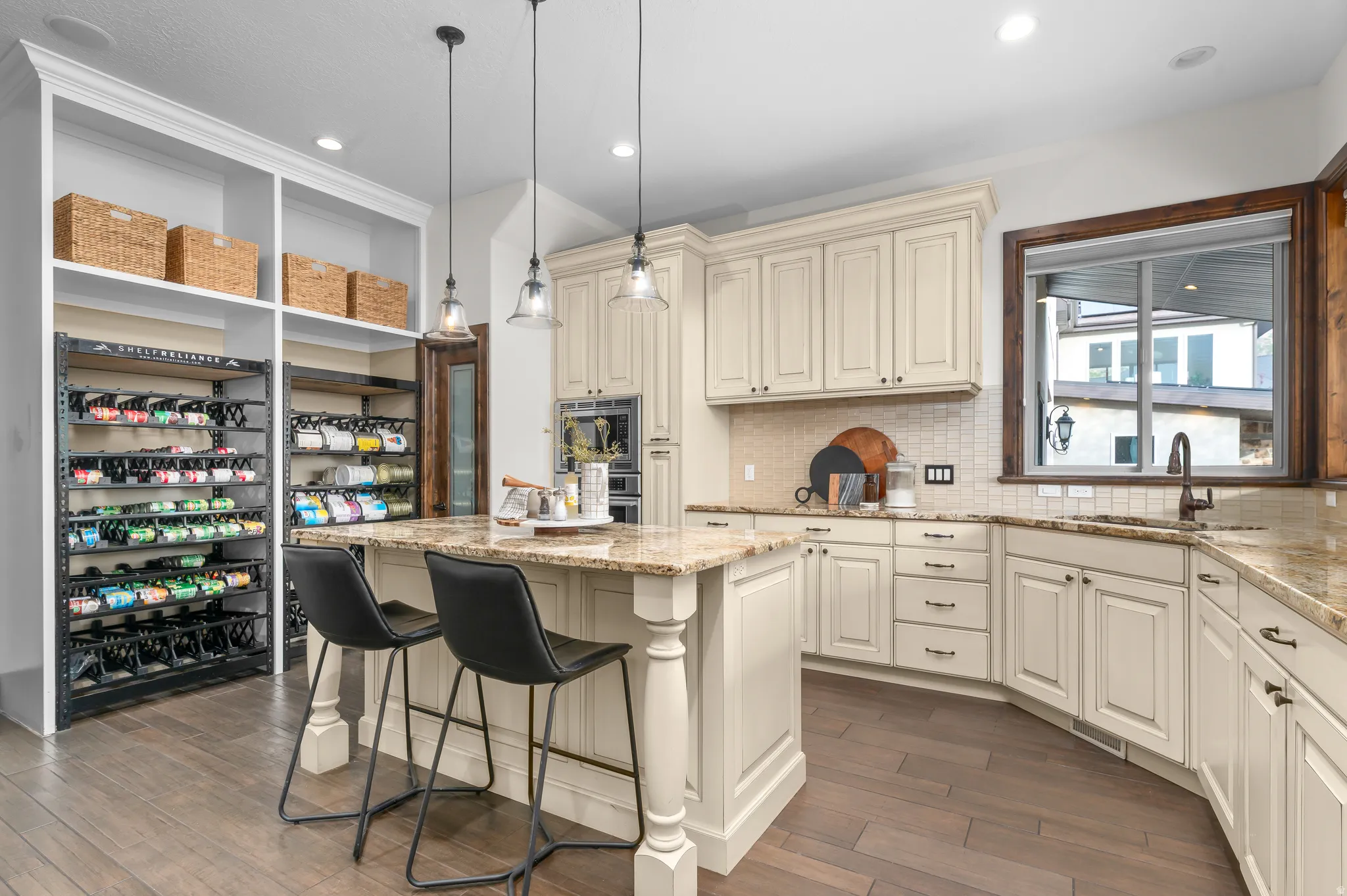 Kitchen featuring granite countertops, cream-painted cabinetry, a large kitchen island with pendant lighting, integrated appliances, and wood-finish flooring