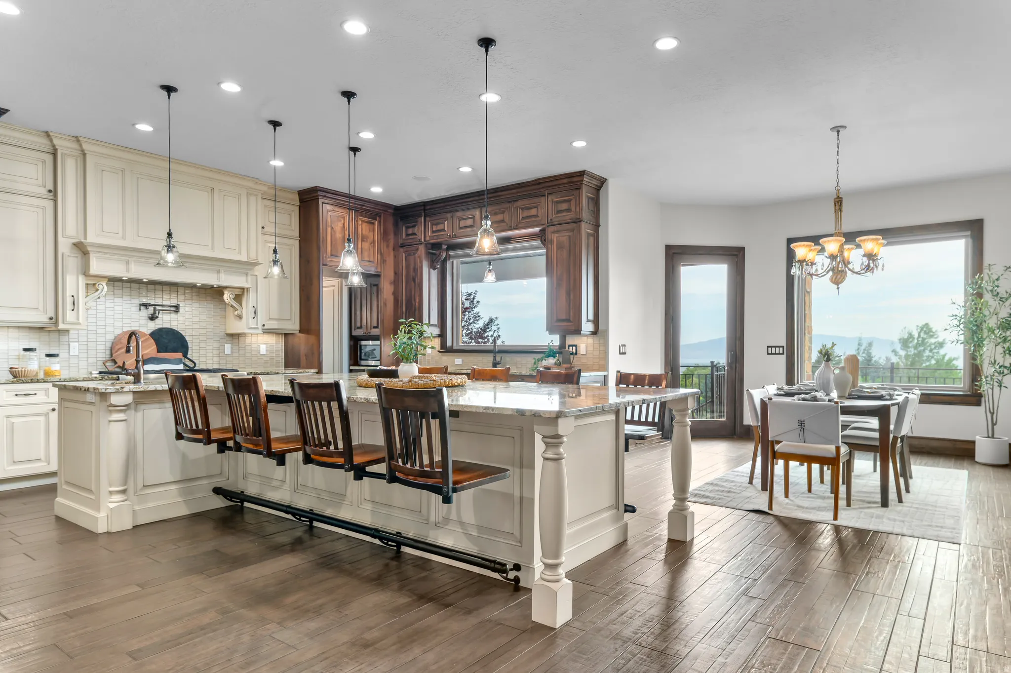 Expansive kitchen island with seating, a mix of light and dark wood cabinetry, recessed lighting, and a dining area with large windows