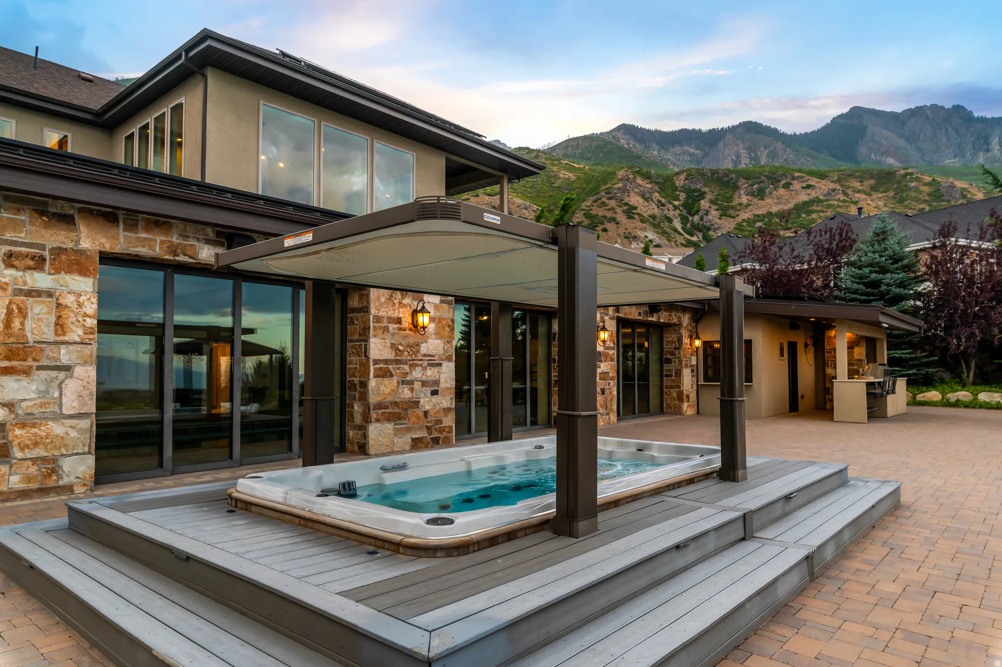 Mountain backdrop, built-in spa with retractable cover, stone and stucco exterior, large sliding glass doors, paver patio