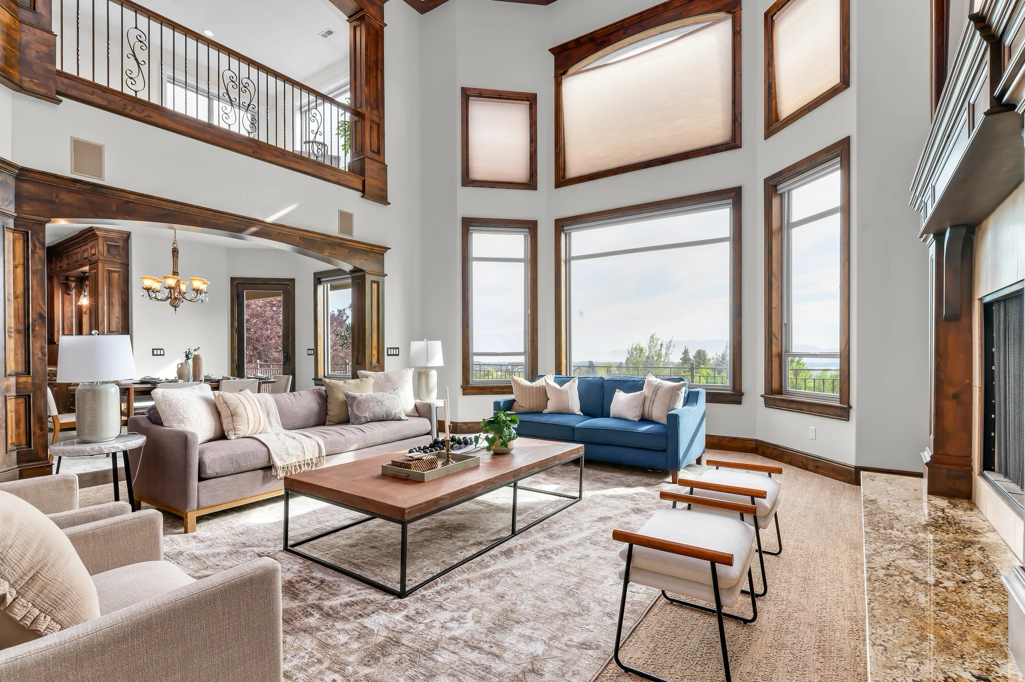 Two-story great room featuring a prominent fireplace with a stone hearth, extensive wood-finish trim and beams, and large windows with transom elements