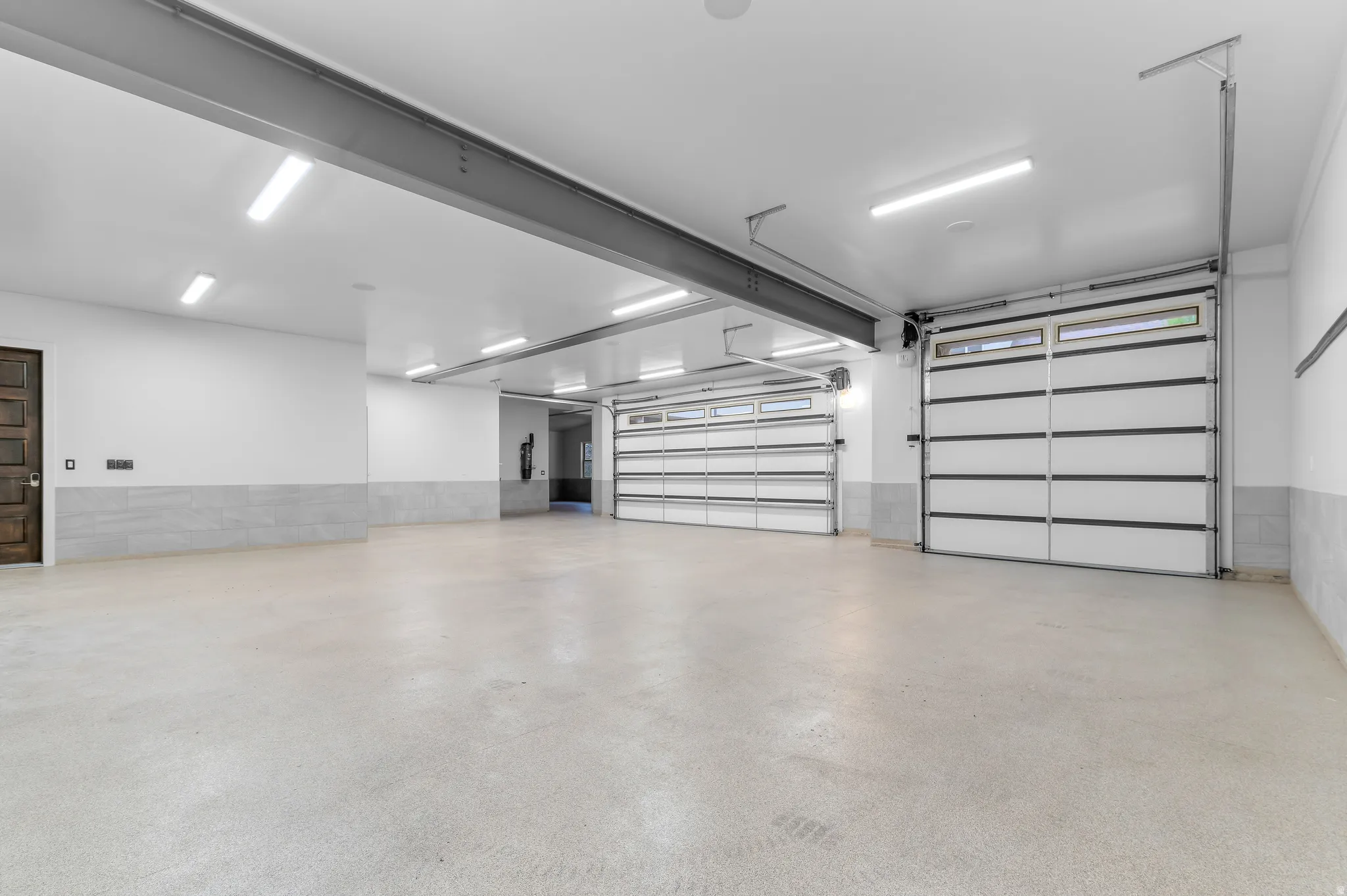 Spacious garage with two overhead doors, featuring high ceilings with exposed structural beams, and a durable epoxy-coated floor