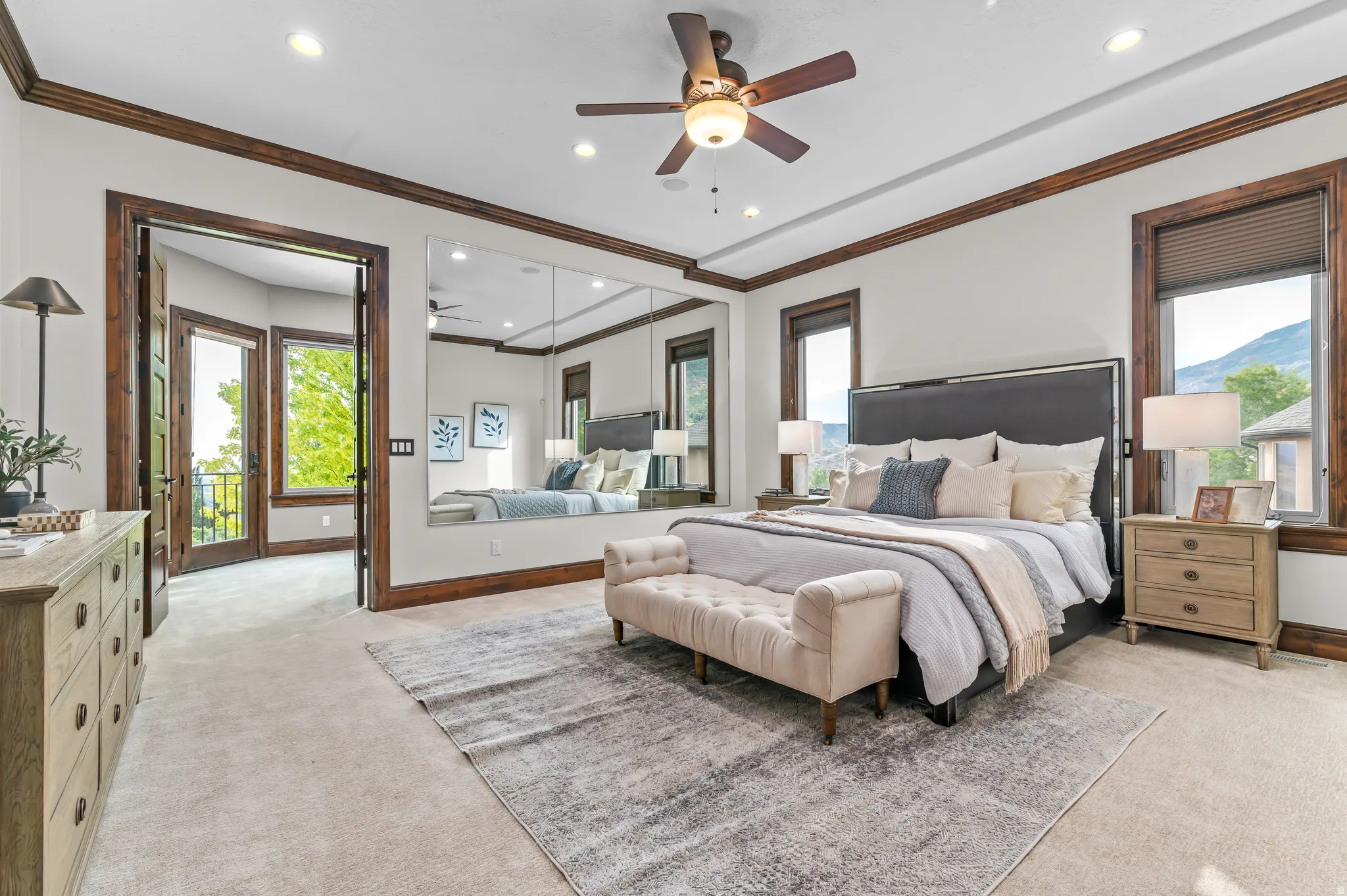 Recessed lighting, ceiling fan with integrated light, custom wood trim, full-height mirrored wall, and dual French doors leading to a balcony