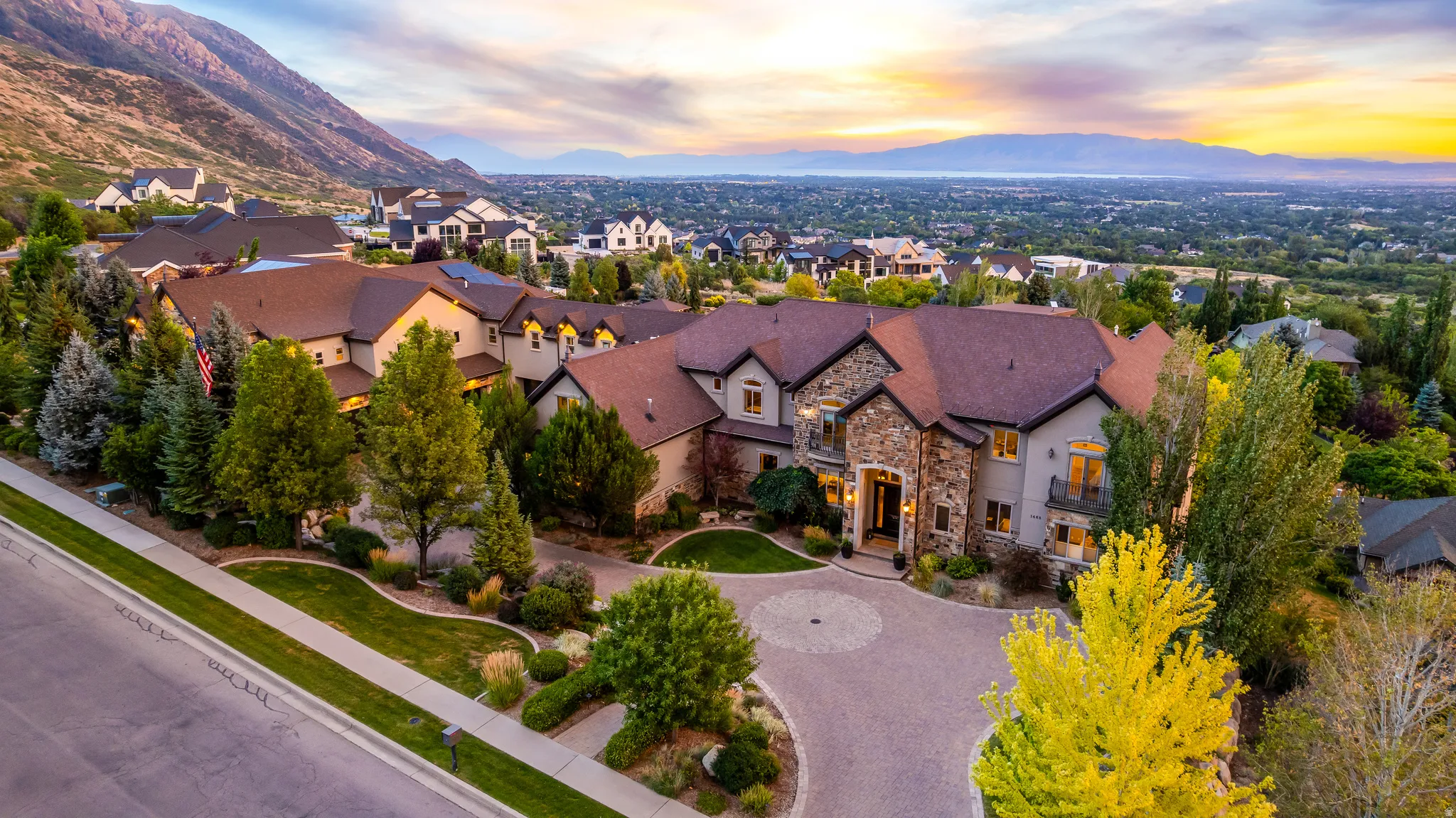 Stone and stucco exterior, multi-level design, paver driveway, mature landscaping, and an expansive mountain backdrop