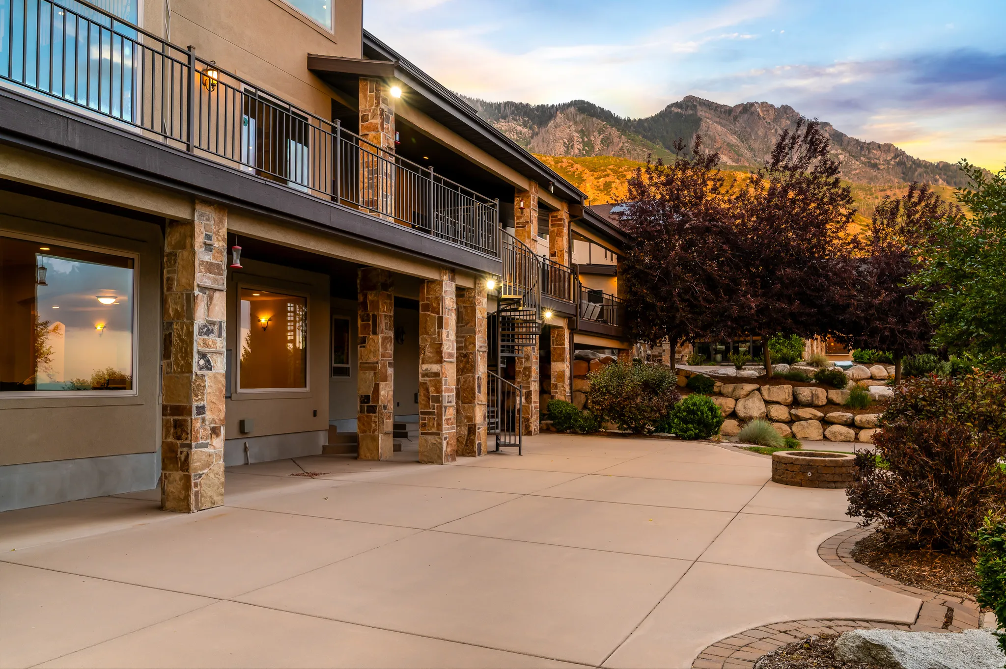Expansive concrete patio with a built-in fire pit, stone-clad columns, and a terraced rock garden