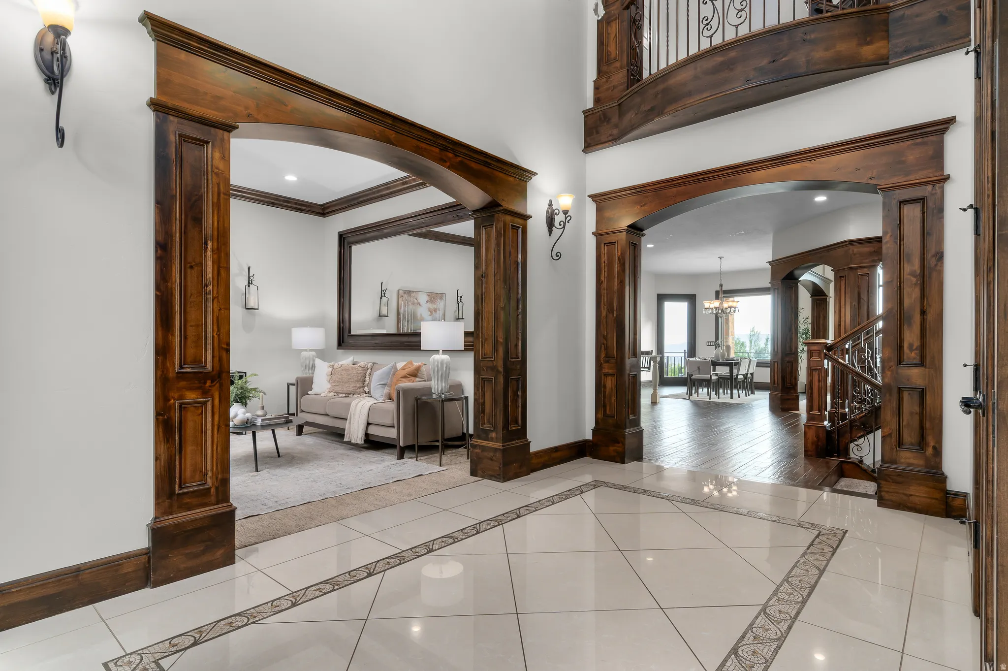 Entryway with large format tile flooring featuring an intricate mosaic border, rich wood-stained arched doorways, and a grand staircase with decorative wrought iron balusters