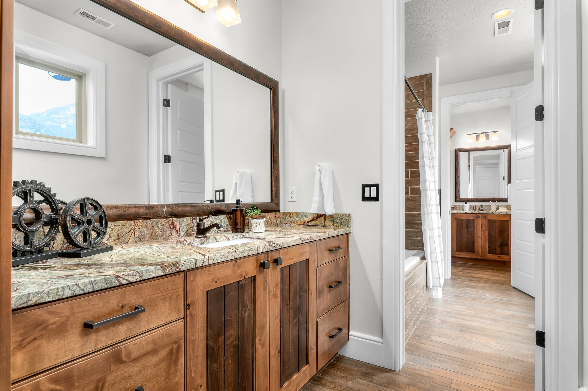 Vanity with wood-finish cabinetry, stone countertop, integrated sink, and an expansive framed mirror