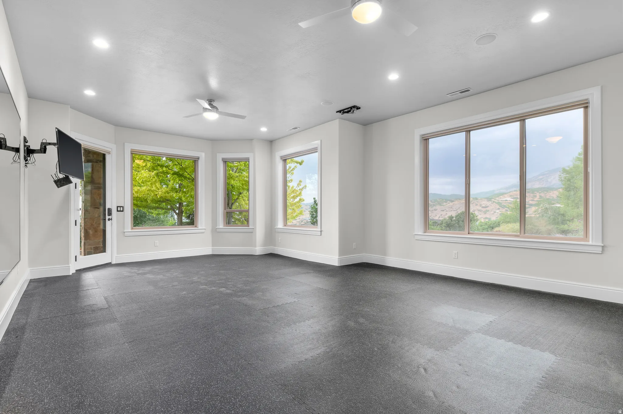 Fitness room, Recessed lighting, ceiling fans, hard surface flooring, multiple large windows, and a glass-paneled door
