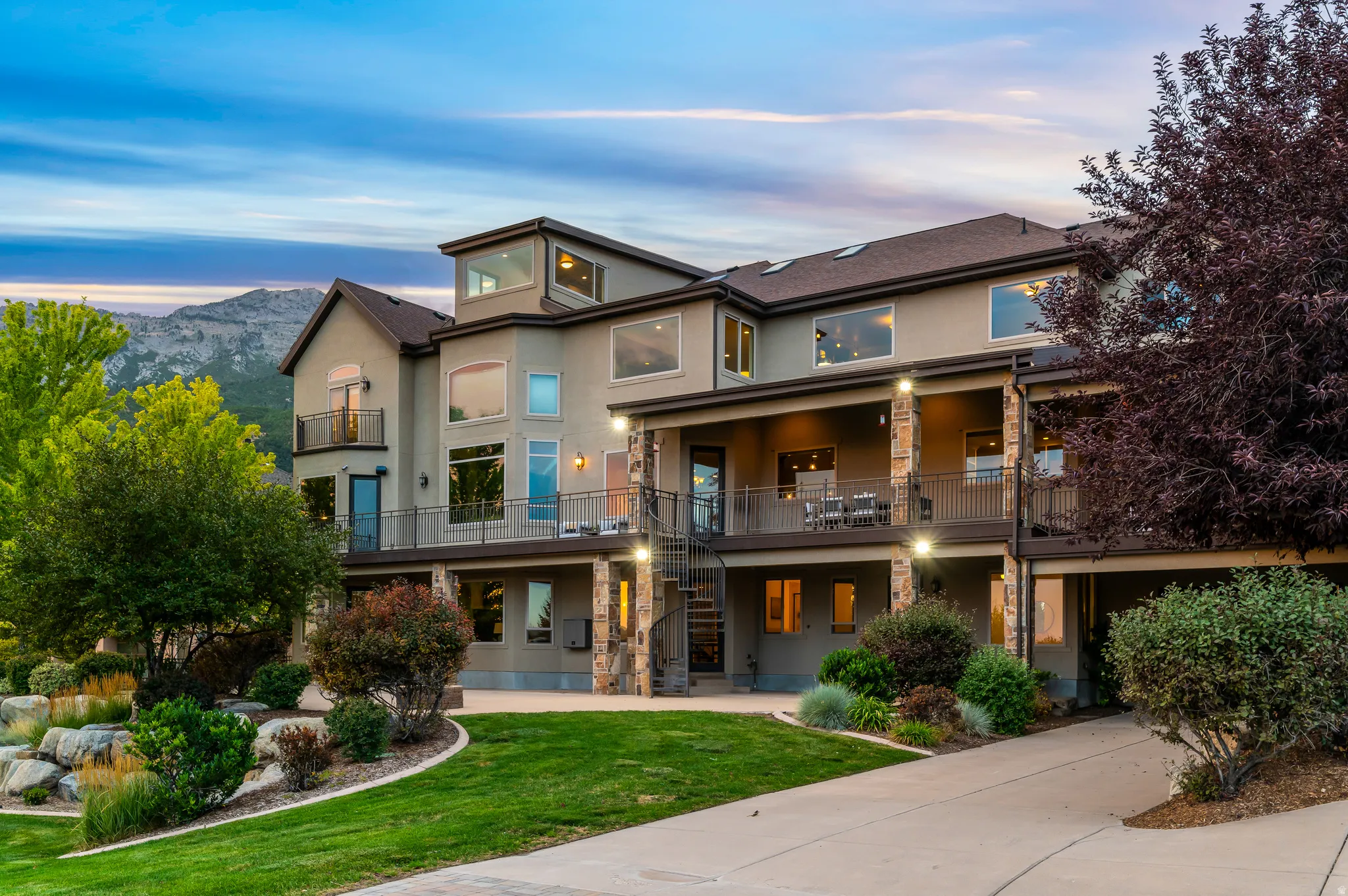 Multi-level stucco exterior with stone accents, multiple balconies, and integrated landscaping with mature trees