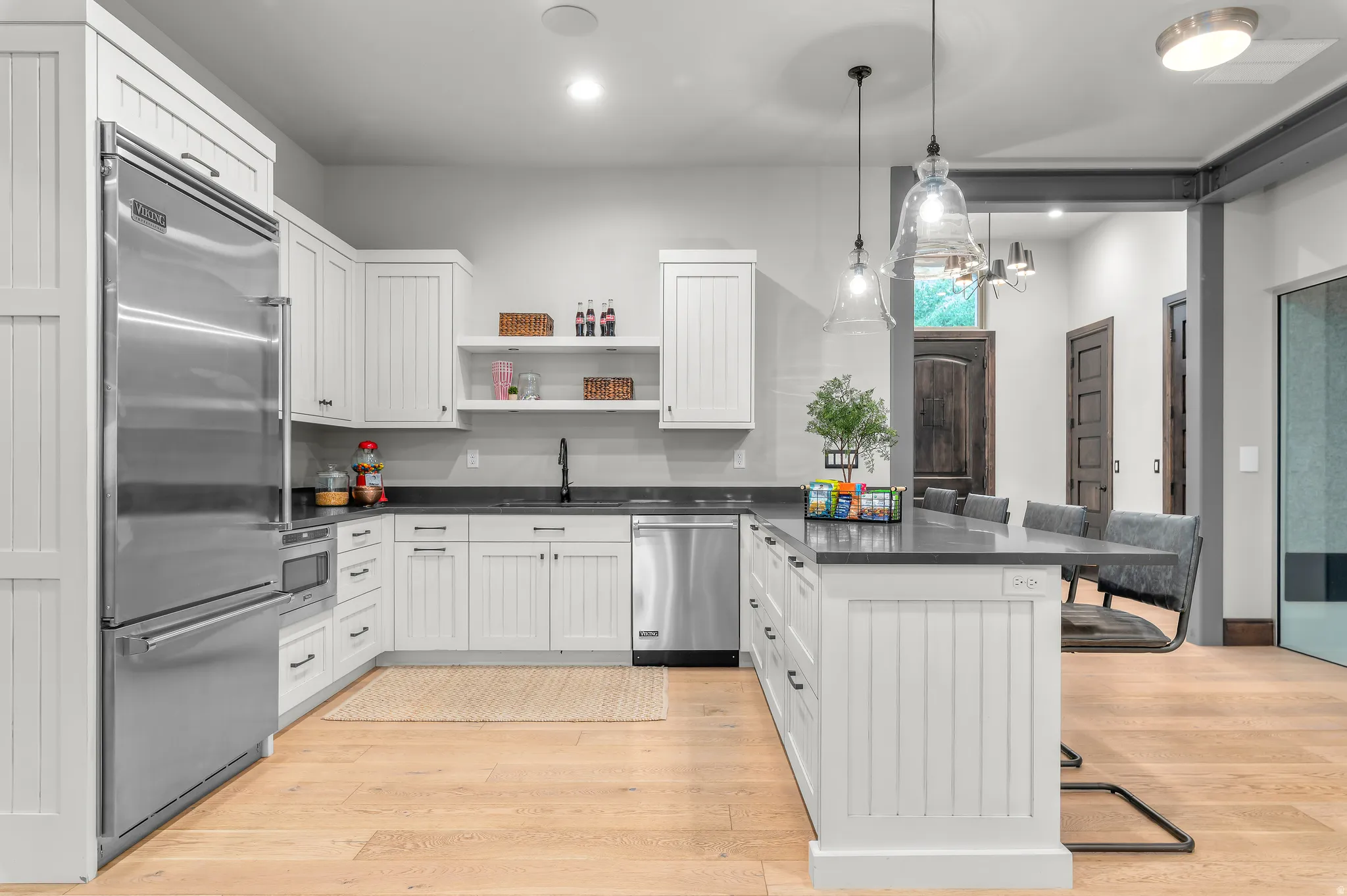 Gourmet kitchen featuring stainless steel appliances, white cabinetry with dark hardware, dark countertops, a central island with seating, and wood-finish flooring